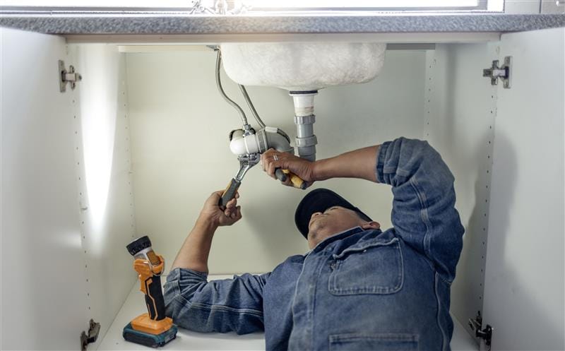 Plumber repairing pipes beneath a bathroom sink in Plant City