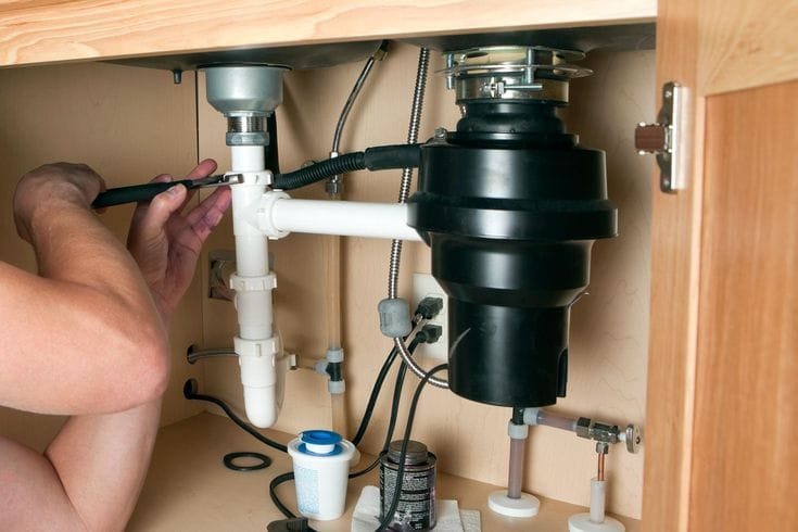 Plumber installing a garbage disposal beneath a kitchen sink in Plant City