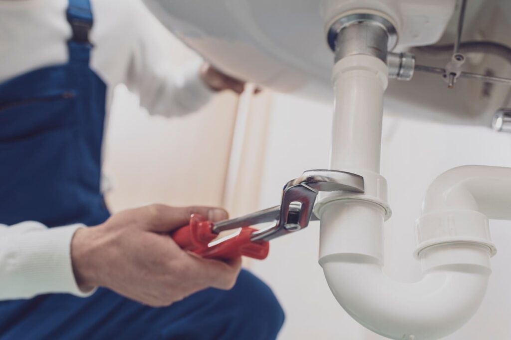Plumber repairing a white drain pipe beneath a sink in Plant City
