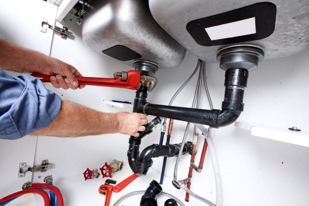 Plumber repairing drain pipes beneath a kitchen sink in Plant City